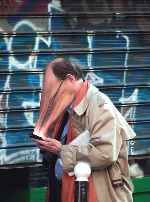Un hombre mira el móvil en la calle, delante de una persiana con grafitis